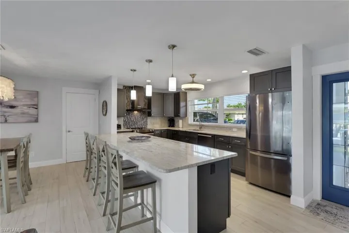 Kitchen featuring stainless steel appliances, a breakfast bar, pendant lighting, light stone counters, and decorative backsplash