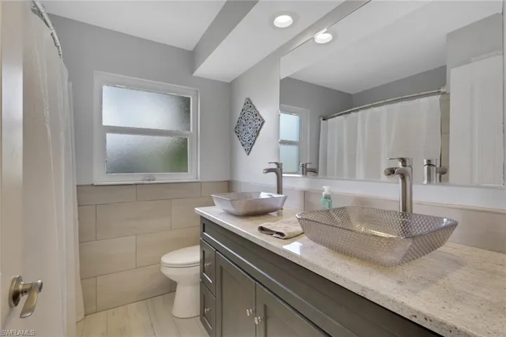 Bathroom featuring tile walls, double vanity, a shower with curtain, wainscoting, and recessed lighting