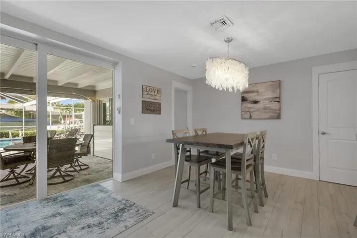 Dining room with light wood-type flooring, a chandelier, a sunroom, and beamed ceiling