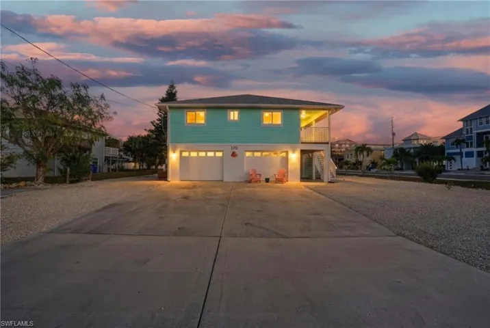 Raised beach house featuring stairway, concrete driveway, a balcony, and a garage - Virtually Edited Image