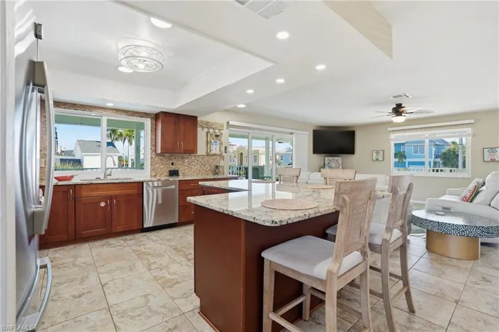 Kitchen featuring light stone countertops, appliances with stainless steel finishes, a center island, a breakfast bar, and recessed lighting - Virtually Edited Image