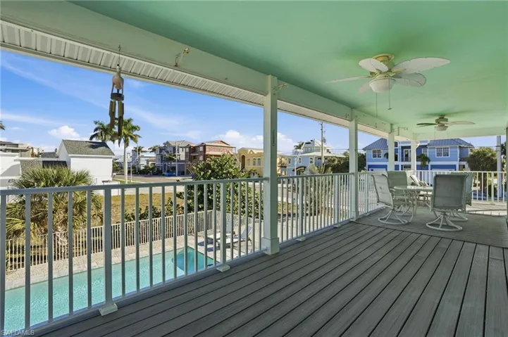 Wooden terrace with a residential view, ceiling fan, outdoor dining space, and a sunroom - Virtually Edited Image