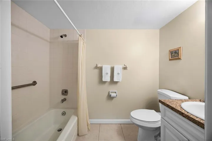 Bathroom featuring shower / bath combo with shower curtain, light tile patterned floors, and vanity