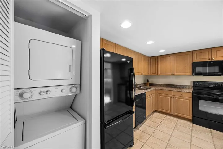 Kitchen featuring black appliances, stacked washer / drying machine, recessed lighting, light tile patterned floors, and light countertops