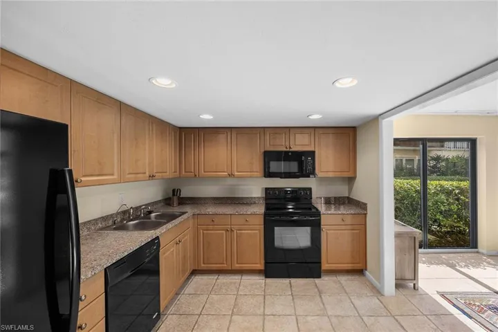 Kitchen featuring black appliances, recessed lighting, light tile patterned floors, brown cabinets, and dark countertops