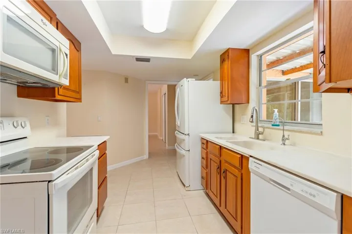 Kitchen featuring a raised ceiling, white appliances, sink, and light tile patterned flooring