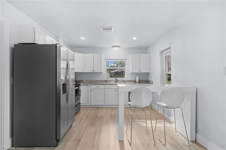 Guest House Kitchen featuring white cabinets, sink, light hardwood / wood-style floors, a kitchen bar, and stainless steel appliances