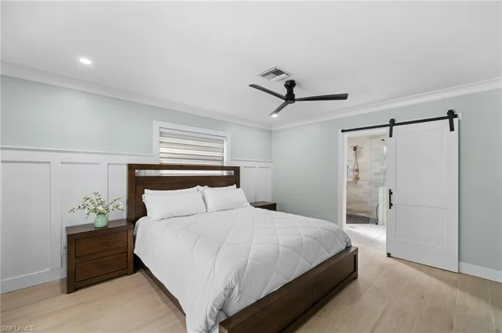 Bedroom with ceiling fan, a barn door, ensuite bathroom, light wood-type flooring, and ornamental molding
