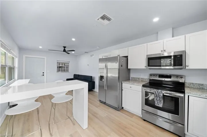 Guest House Kitchen featuring white cabinetry, ceiling fan, stainless steel appliances, a breakfast bar, and light wood-type flooring