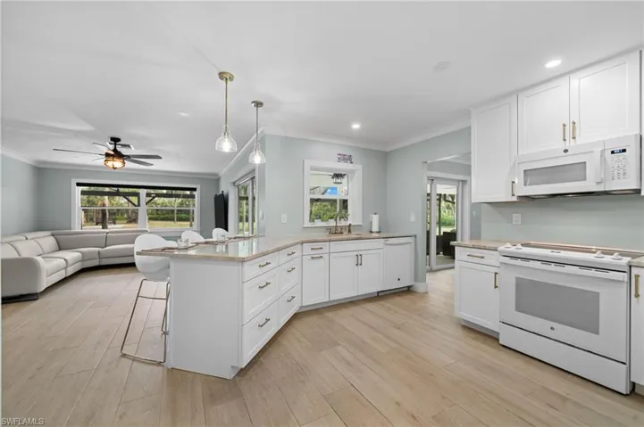 Open Concept Kitchen with white appliances, crown molding, pendant lighting, light hardwood / wood-style flooring, and white cabinetry