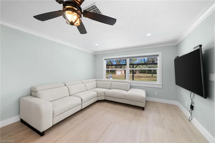 Living room with ceiling fan, light wood-type flooring, and crown molding