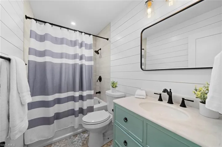 Full bathroom featuring vanity, toilet, shower / bathtub combination with curtain, and wooden walls
