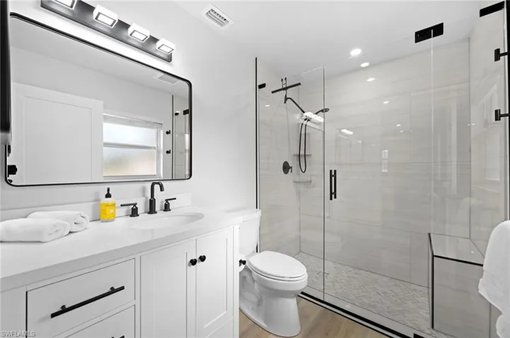 Guest House Bathroom with a shower with door, vanity, wood-type flooring, and toilet