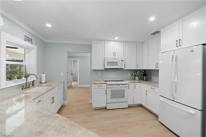 Kitchen featuring light stone countertops, white appliances, sink, light hardwood / wood-style floors, and white cabinetry