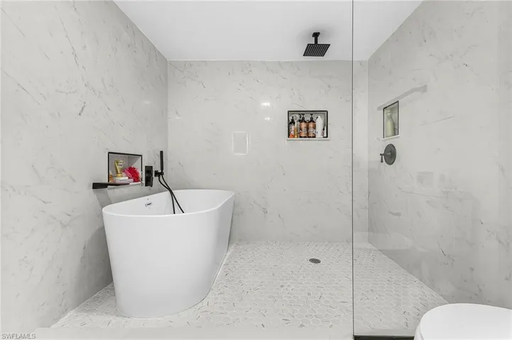 Full bath featuring a marble finish shower, a soaking tub, stone wall, and tile walls