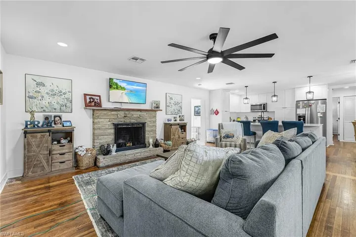 Living room with a ceiling fan, dark wood-type flooring, a stone fireplace, and recessed lighting