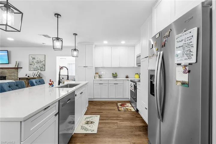 Kitchen featuring stainless steel appliances, white cabinetry, hanging light fixtures, dark wood-type flooring, and open floor plan