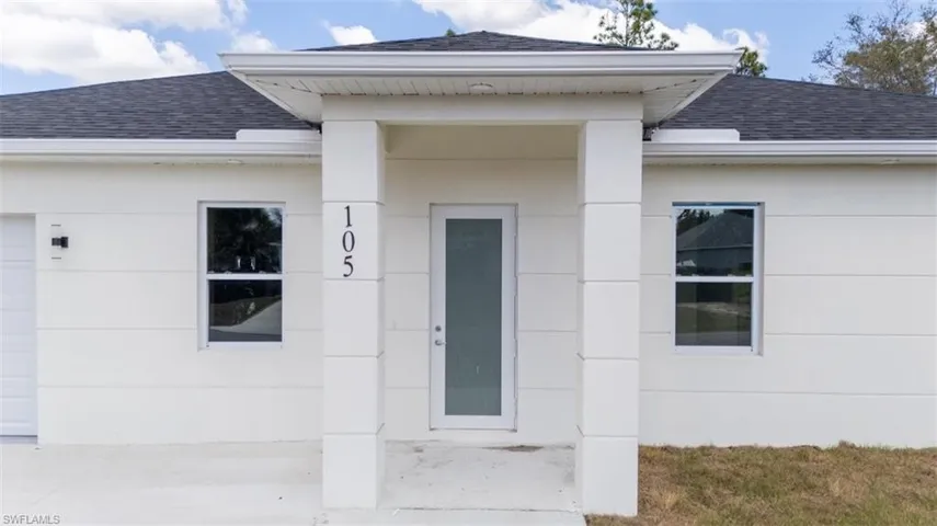 Entrance to property with a shingled roof, covered porch, stucco siding, and a garage