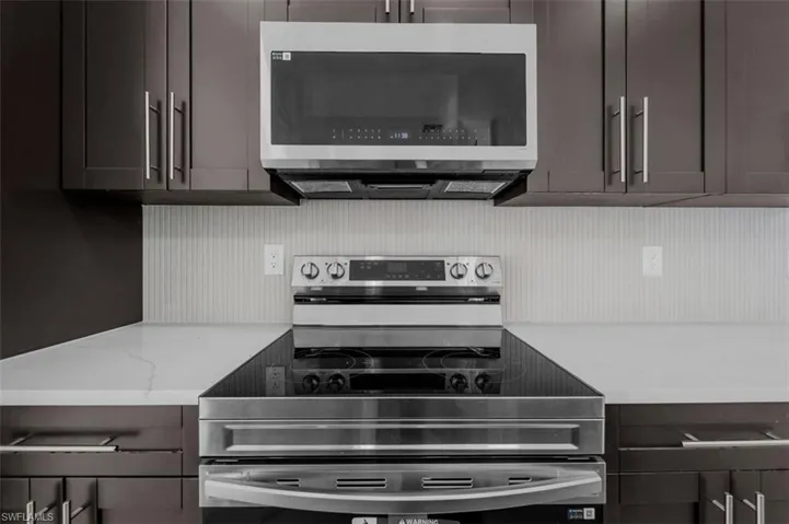 Kitchen featuring stainless steel appliances, light stone countertops, and dark wood finish cabinets