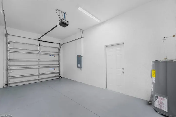 Garage with water heater, electric panel, and a garage door opener