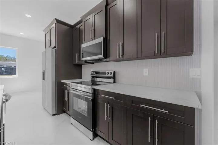 Kitchen featuring stainless steel appliances, dark wood finish cabinetry, light stone counters, and recessed lighting