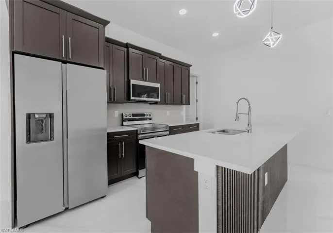 Kitchen with stainless steel appliances, a kitchen island with sink, dark wood finish cabinets, hanging light fixtures, and light stone countertops