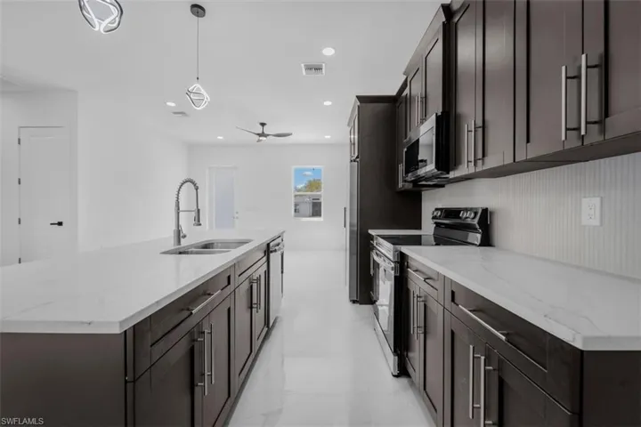 Kitchen featuring stainless steel appliances, a center island with sink, pendant lighting, dark wood finish cabinets, and light stone countertops