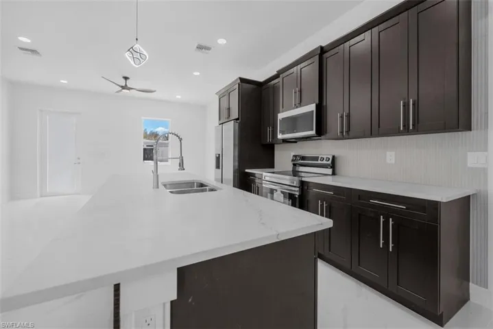Kitchen featuring stainless steel appliances, a breakfast bar area, light stone counters, an island with sink, and dark wood finish cabinetry