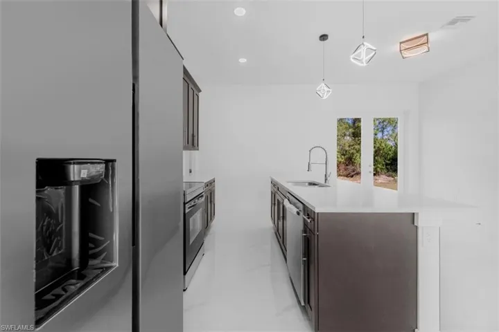 Kitchen with stainless steel appliances, a kitchen island with sink, dark wood finish cabinets, and hanging light fixtures