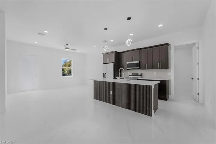 Kitchen featuring an island with sink, decorative light fixtures, dark wood finish cabinets, stainless steel appliances, and a ceiling fan