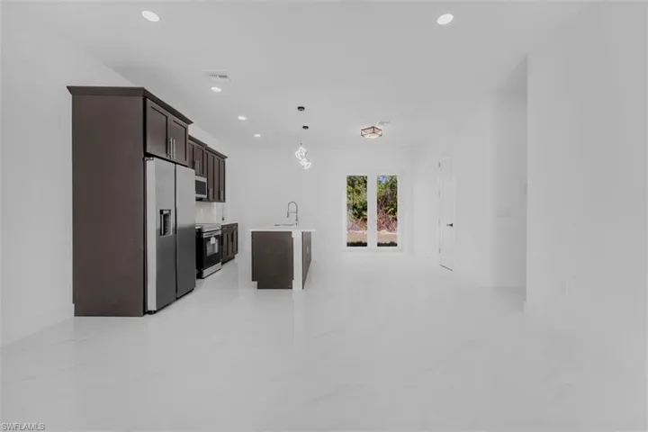 Kitchen featuring an island with sink, dark wood finish cabinetry, stainless steel appliances, decorative light fixtures, and open floor plan