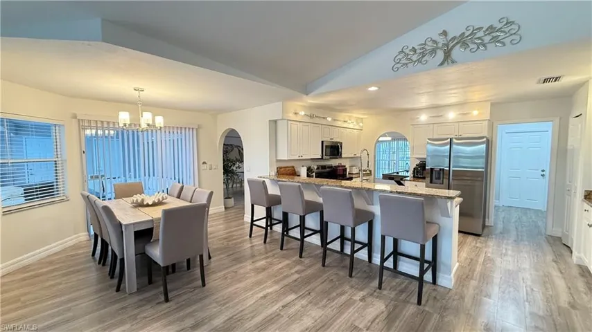 Dining space featuring arched walkways, lofted ceiling, light wood-type flooring, and a chandelier