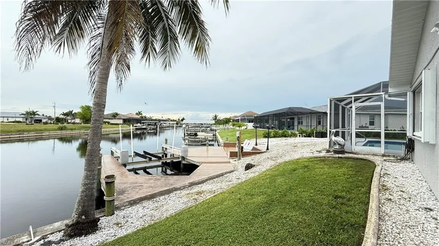 Dock area featuring glass enclosure, boat lift, a sunroom, a water view, and a lawn