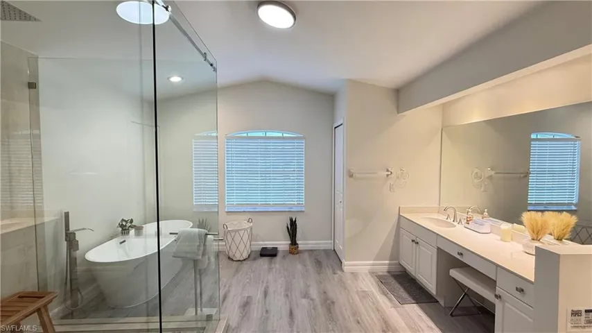 Bathroom featuring vanity, light wood-style flooring, a freestanding bath, vaulted ceiling, and a shower with shower door