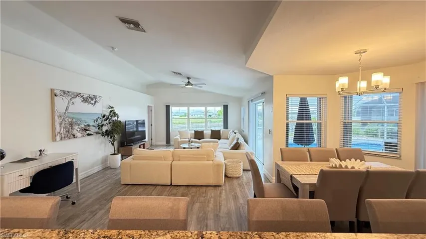 Living area featuring lofted ceiling, a chandelier, wood finished floors, and ceiling fan
