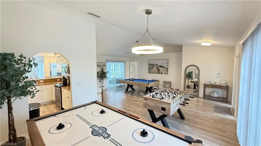 Rec room with vaulted ceiling, billiards table, light wood-style flooring, and arched walkways
