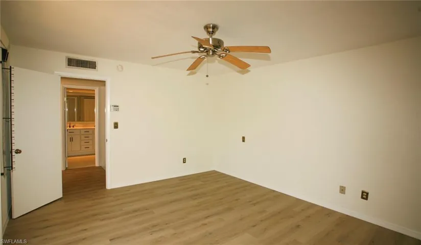 Spacious room featuring wood-finish flooring, a ceiling fan with light, and a dedicated entrance to a bathroom with a white vanity and countertop