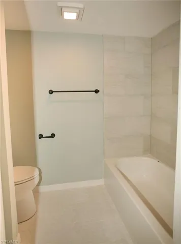 Bathroom featuring a white bathtub, light-toned wall tile, and hexagonal floor tiles