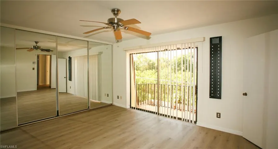 Spacious room featuring wood-finish flooring, a ceiling fan with light fixture, and mirrored closet doors