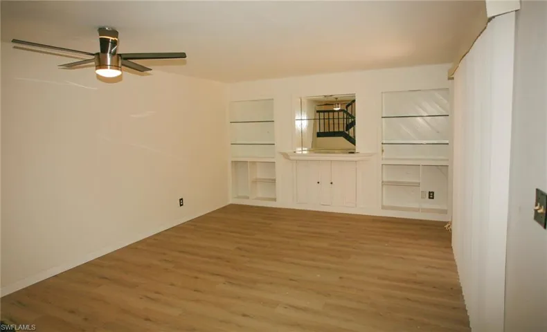 Spacious room featuring wood-finish flooring, a modern ceiling fan with integrated lighting, and white walls