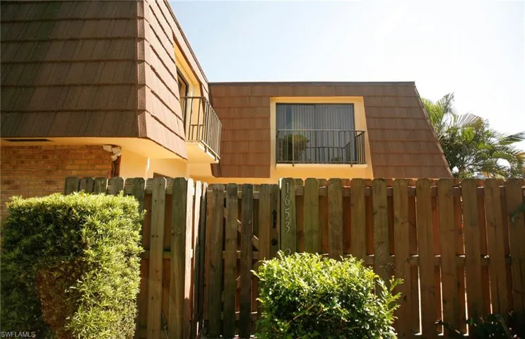 Exterior featuring a privacy fence, balcony with metal railing, and a window with blinds