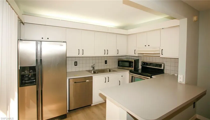 Kitchen featuring white cabinetry, stainless steel refrigerator, stainless steel dishwasher, electric range, and a breakfast bar with a solid surface countertop