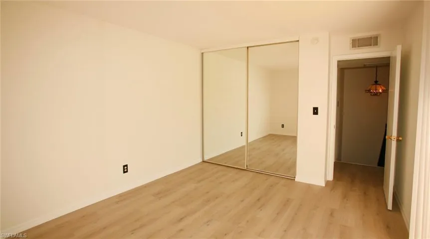 Spacious room featuring light wood-finish flooring and a full wall of mirrored closet doors