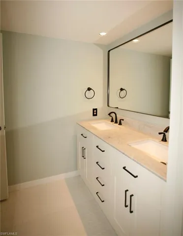 Double vanity with white shaker-style cabinetry and matte black hardware, featuring dual undermount sinks and a light-toned stone countertop