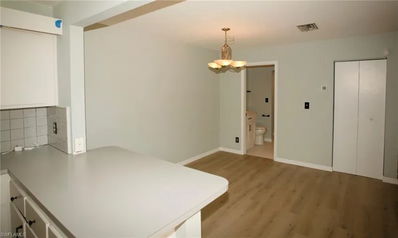 Open concept area featuring light-toned walls, wood-finish flooring, a contemporary ceiling light fixture, a breakfast bar with a solid surface countertop, and bi-fold closet doors