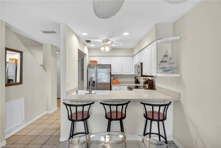 Kitchen with a breakfast bar, light countertops, light tile patterned floors, white cabinetry, and appliances with stainless steel finishes