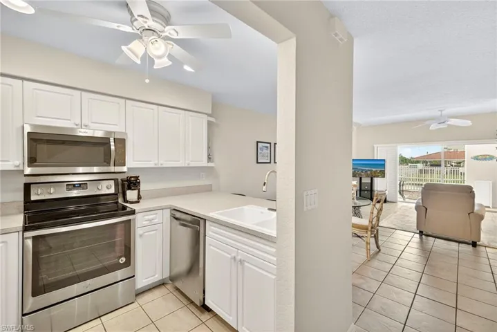Kitchen featuring ceiling fan, stainless steel appliances, light tile patterned floors, open floor plan, and white cabinetry