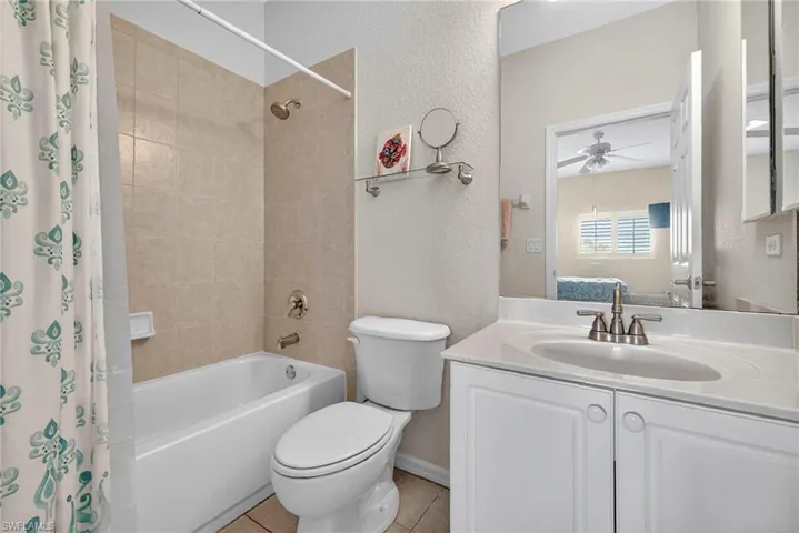 Full bath featuring a textured wall, shower / bath combination with curtain, vanity, light tile patterned floors, and ceiling fan