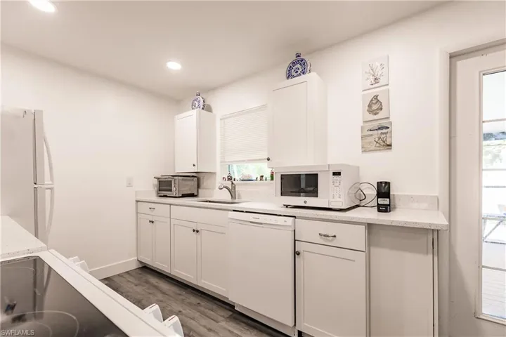Kitchen with white appliances, light wood-style floors, white cabinets, light stone countertops, and recessed lighting