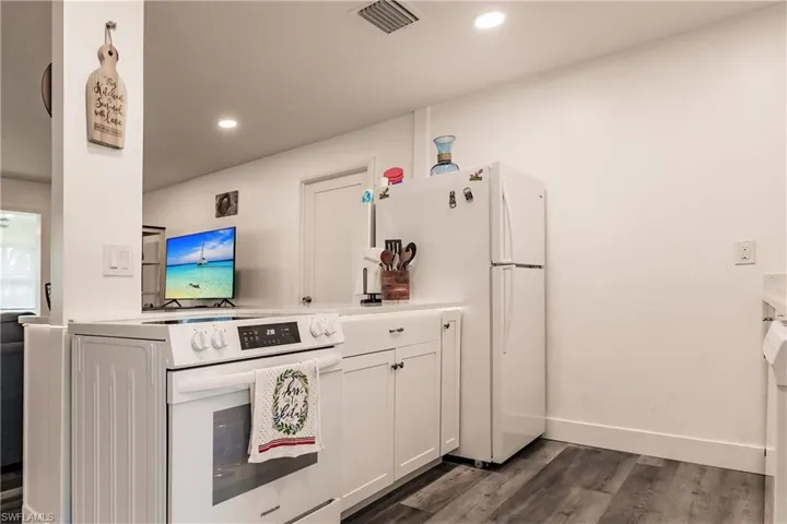 Kitchen with white appliances, white cabinetry, light countertops, dark wood-style floors, and recessed lighting
